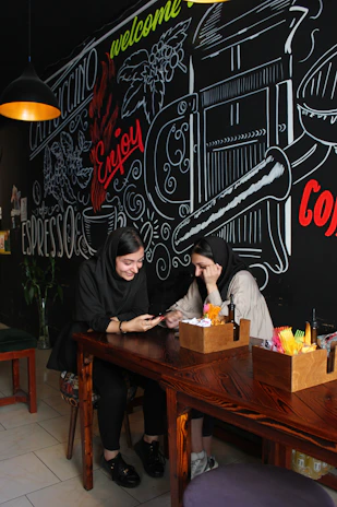 A cozy café setting with two people laughing over coffee and a tablet showing date options.