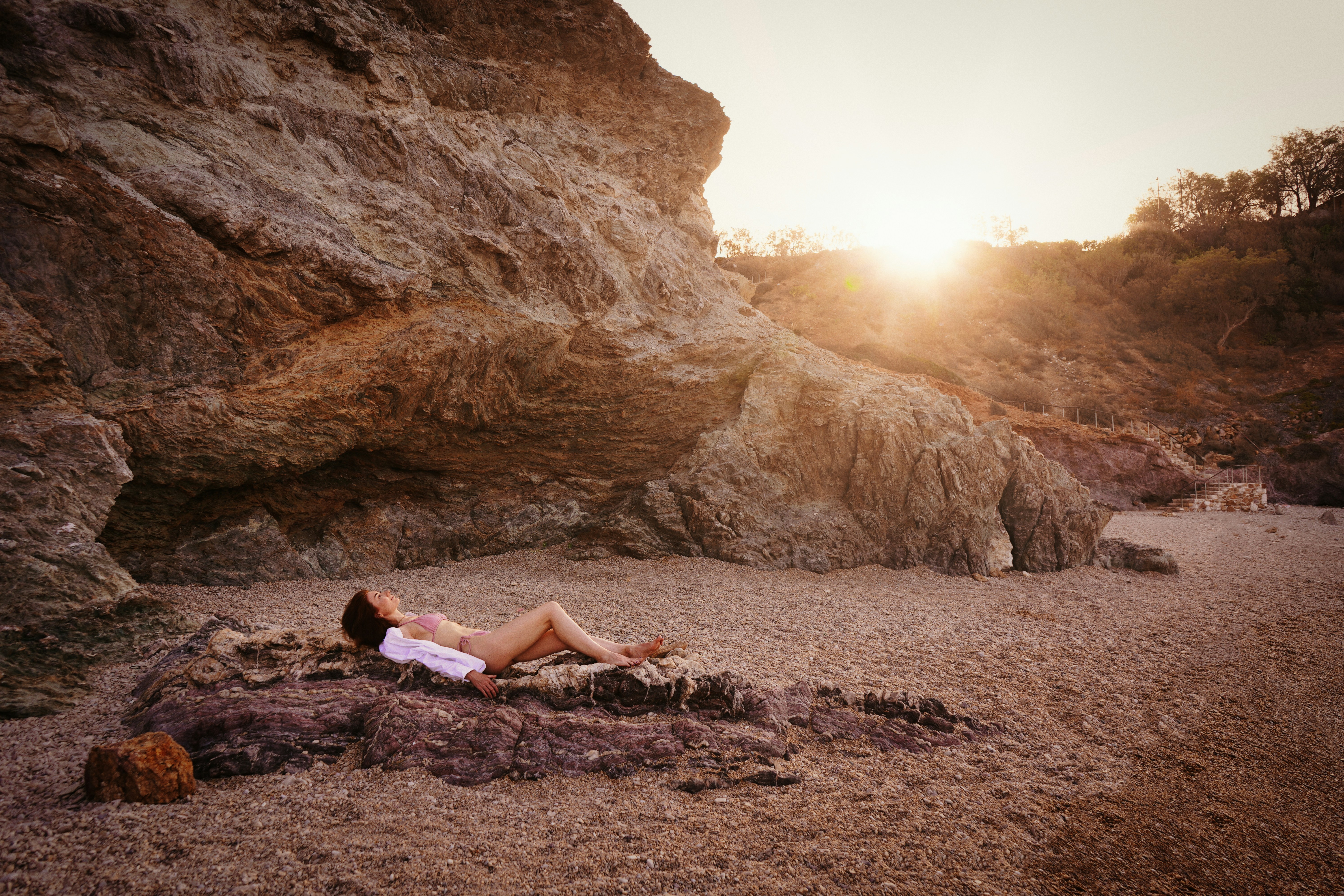 a woman laying on the ground next to a large rock