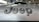 Close-up view of a car hood with the word 'Jeep' prominently displayed in dark, bold letters. The background shows an indoor car showroom with other vehicles and showroom decor.