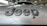 Close-up view of a car hood with the word 'Jeep' prominently displayed in dark, bold letters. The background shows an indoor car showroom with other vehicles and showroom decor.