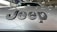Close-up view of a car hood with the word 'Jeep' prominently displayed in dark, bold letters. The background shows an indoor car showroom with other vehicles and showroom decor.