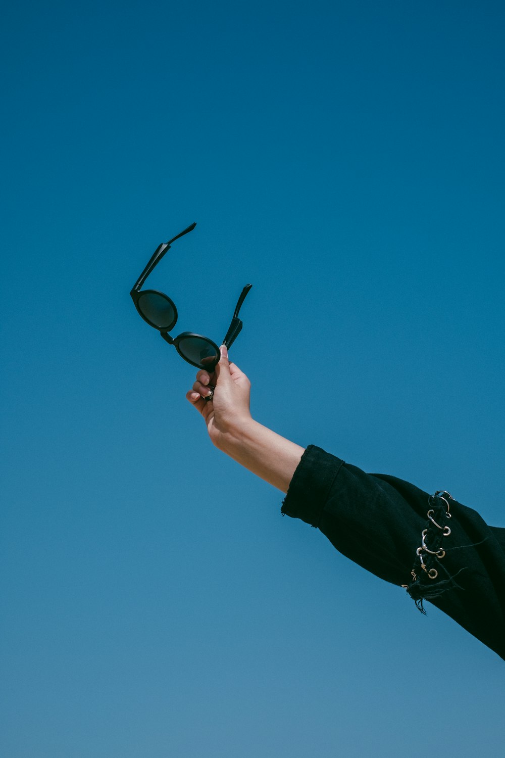 a hand holding up a pair of sunglasses against a blue sky