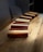 Rectangular wooden blocks are arranged diagonally on a wooden table. Each block features a polished finish with contrasting light and dark wood stripes. The table has a visible grain pattern and there is a cushion in the background.