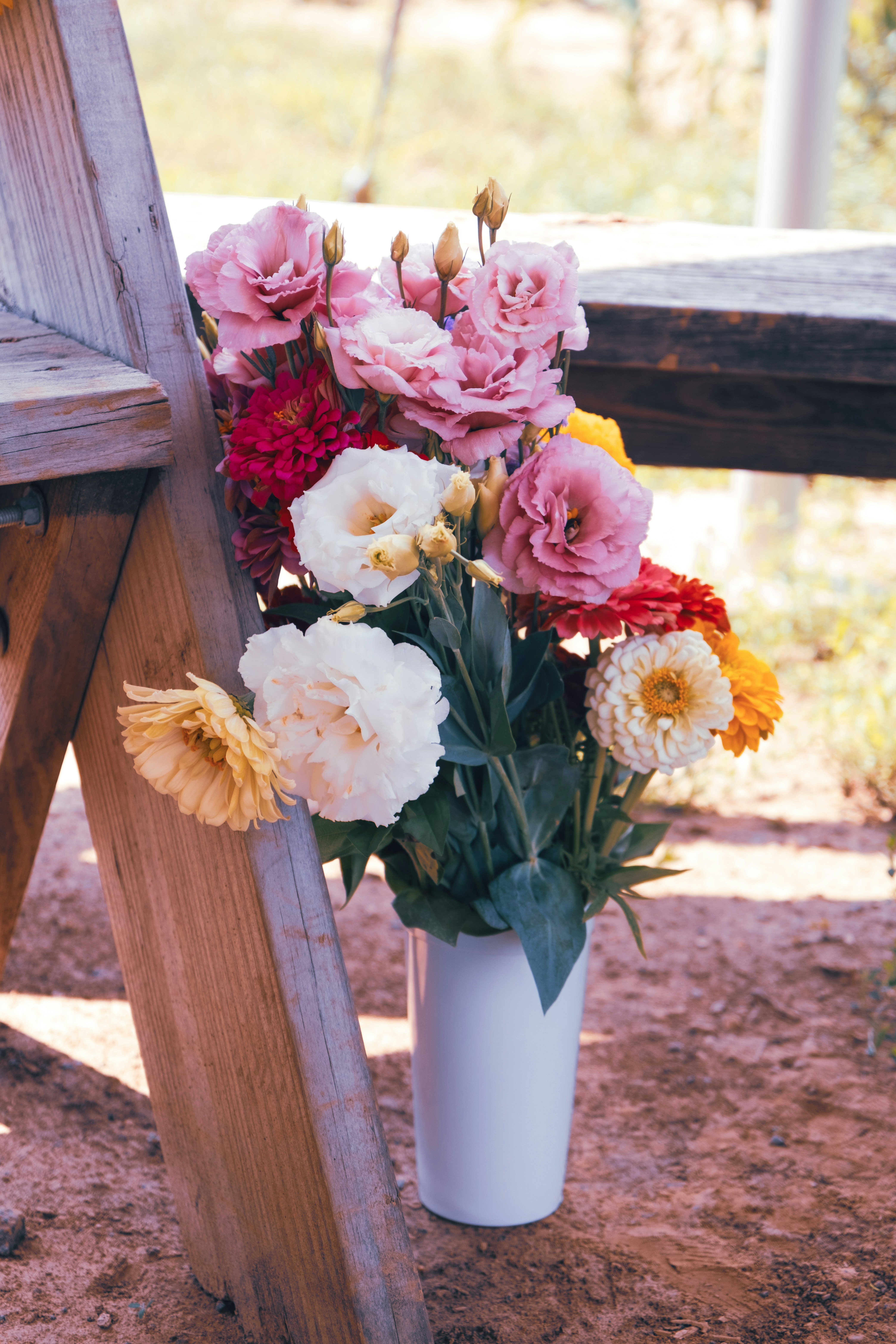 a white vase filled with lots of flowers next to a wooden bench