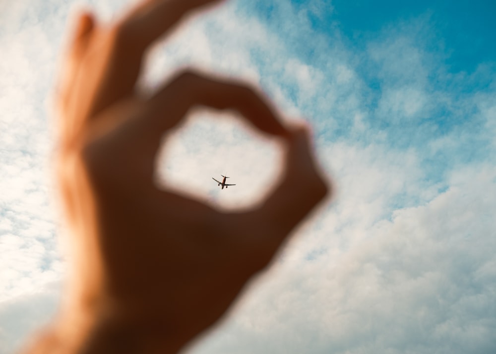a hand making a heart shape with an airplane in the background