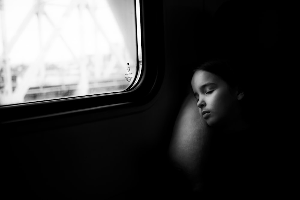a woman sleeping on a train next to a window