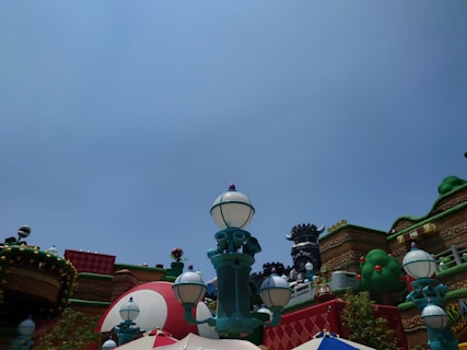 A whimsical scene with large cartoonish street lamps, oversized trees, and vibrant structures with playful designs. The environment has elements resembling a fantasy theme park with colorful decorations.