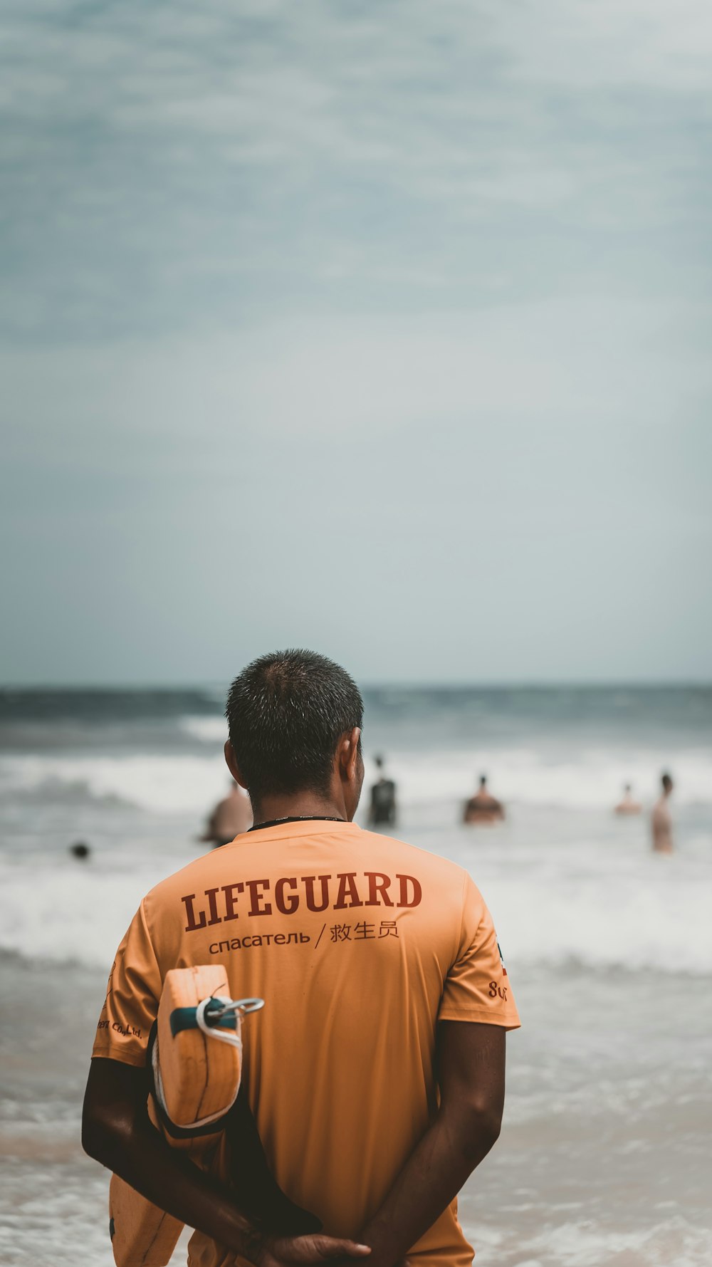 a man in an orange lifeguard shirt standing on the beach