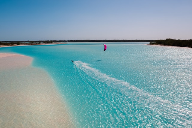 A vibrant scene of a kitesurfer gliding over turquoise water with a clear blue sky.