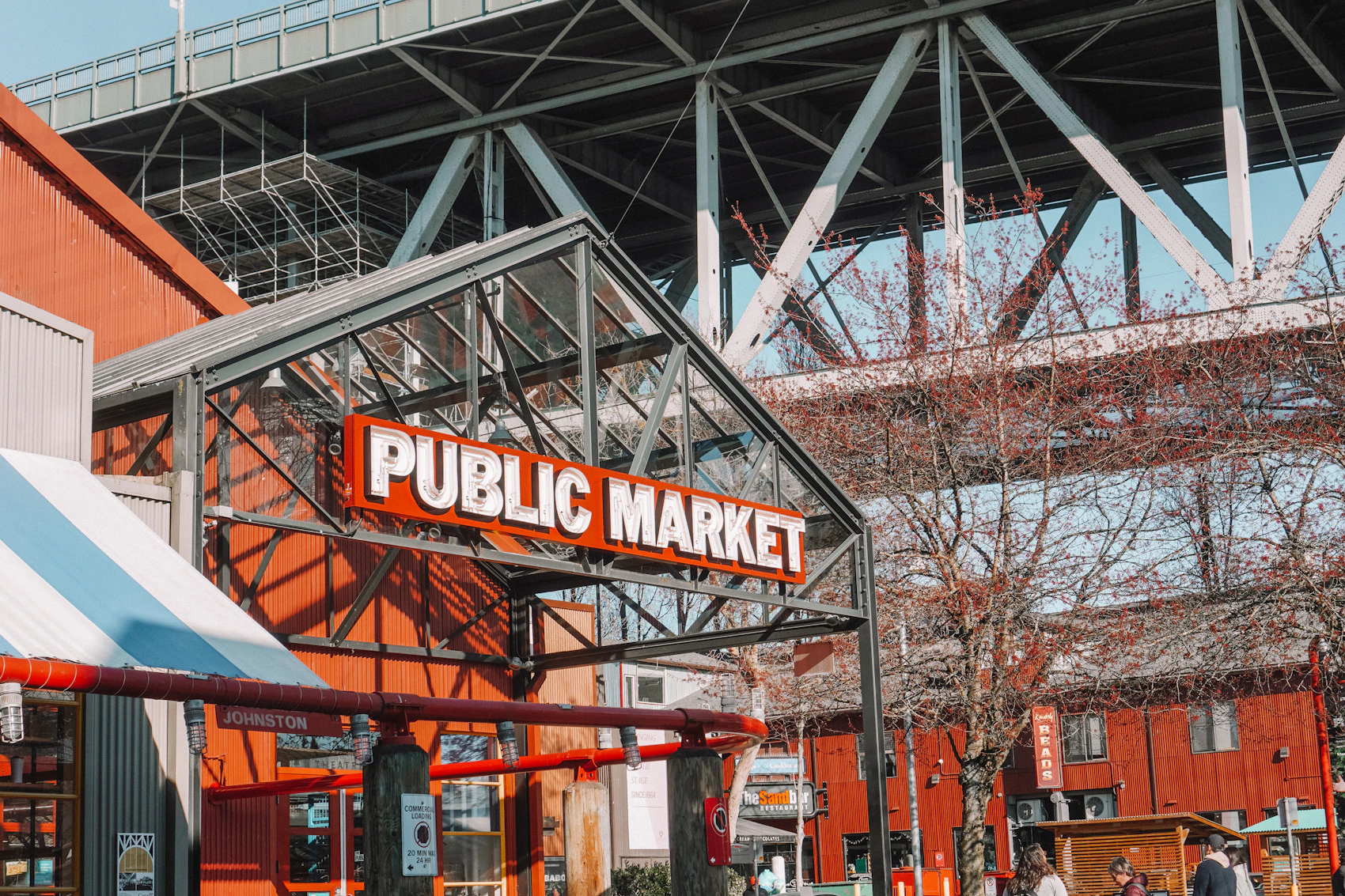 The red entrance of Granville Island Public Market beneath a steel bridge