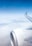 An airplane wing and engine are visible against a backdrop of a clear blue sky and a layer of clouds below. The tip of the wing features branding from an airline, suggesting that the aircraft is mid-flight at a high altitude.