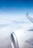 An airplane wing and engine are visible against a backdrop of a clear blue sky and a layer of clouds below. The tip of the wing features branding from an airline, suggesting that the aircraft is mid-flight at a high altitude.