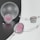 A composition of elegant jewelry pieces featuring pastel pinks and silver tones. Delicate strings of pearls and beads are artfully arranged around smooth, translucent orbs and geometric shapes, reflecting light on a neutral background.