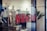 Red letters spelling 'NEW IN' are prominently displayed on a glass window, hinting at the entrance to a retail store. Inside, mannequins and display racks featuring clothing items can be seen, indicating a fashion shop setup. Blurred elements and reflections add depth to the scene.