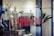 Red letters spelling 'NEW IN' are prominently displayed on a glass window, hinting at the entrance to a retail store. Inside, mannequins and display racks featuring clothing items can be seen, indicating a fashion shop setup. Blurred elements and reflections add depth to the scene.