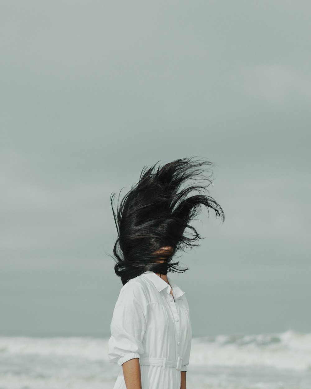a woman standing on a beach with her hair in the wind