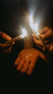 A warm circle of hands joined together in prayer around a softly glowing candle.