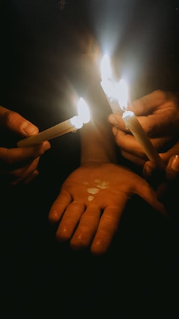 Close-up of hands raised in unity, holding candles during an evening gathering.