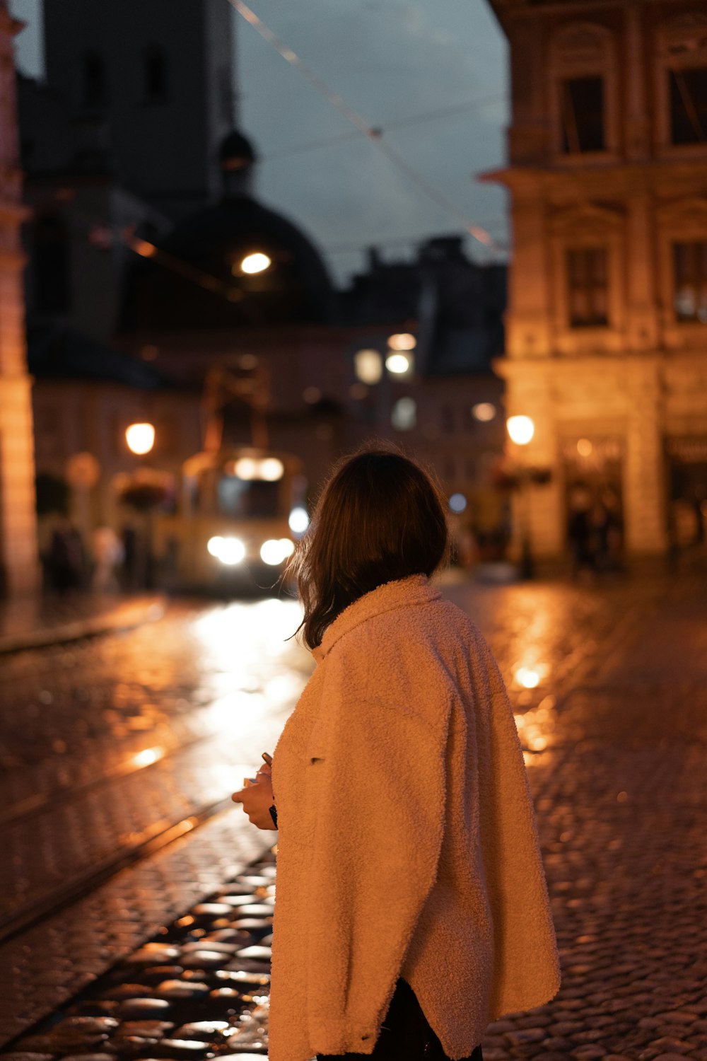 a woman standing on a cobblestone street at night