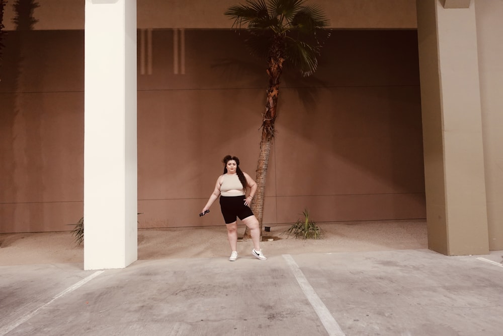 a woman standing in a parking lot next to a palm tree