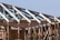 A partially constructed wooden framework of a building under a clear blue sky. The structure consists of exposed beams and trusses, showing the skeletal form of the roof and walls. Metal connectors are visible at the joints, enhancing the structural integrity.