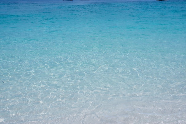 Crystal-clear turquoise waters gently lapping against a white sandy beach at sunrise.