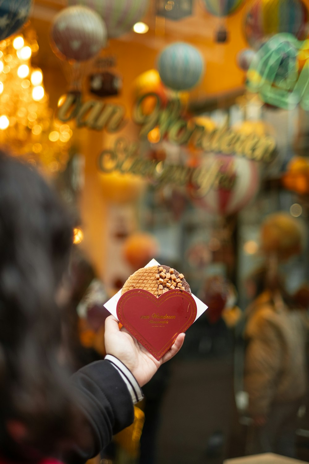 a person holding a heart shaped pastry in front of a store window