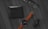 A flat lay arrangement on a wooden surface includes a black leather wallet, a pair of black-framed glasses, a watch with a brown leather strap and black face, and a black rectangular case with a logo. The items are neatly organized, creating a minimalist and professional look.