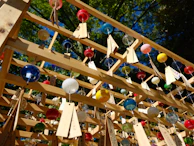 An outdoor scene showing colorful beaded sun catchers hanging from tree branches, swaying gently in the breeze.