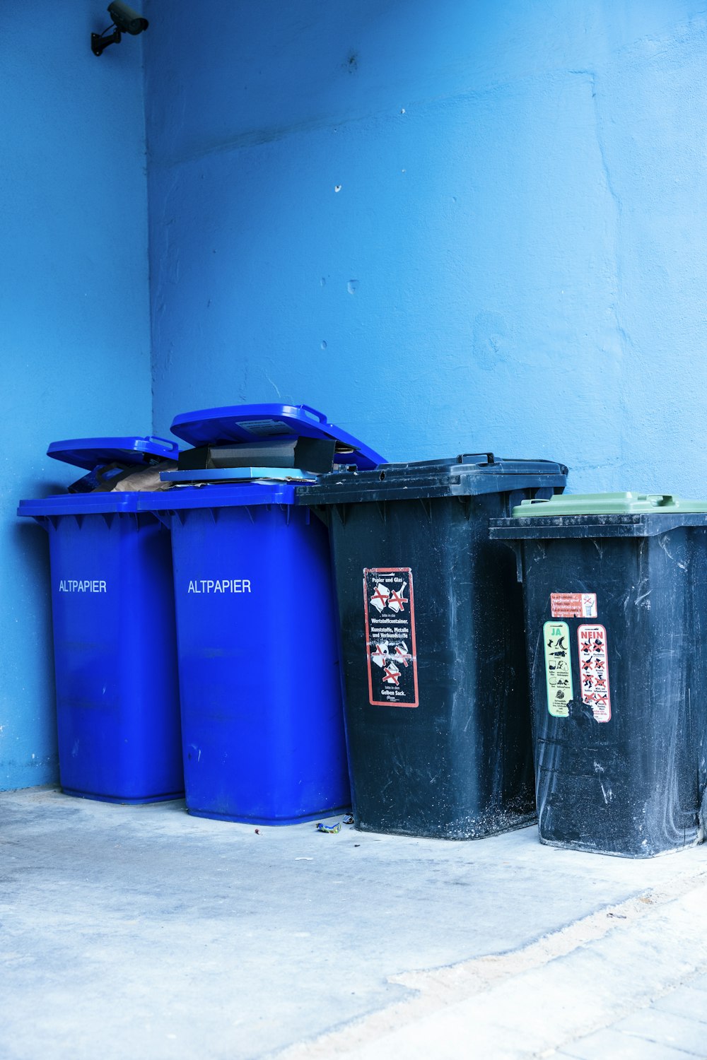 three blue trash cans sitting next to a blue wall