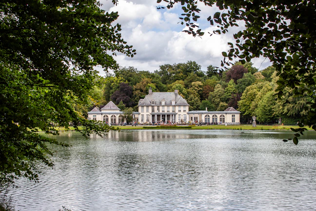 Elegant modern mansion with floor-to-ceiling windows overlooking a serene lake at sunset.