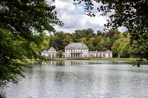 Elegant modern mansion with floor-to-ceiling windows overlooking a serene lake at sunset.