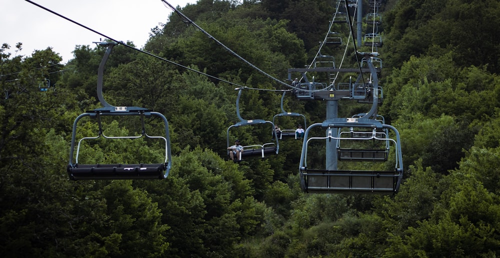 a couple of people riding a ski lift over a forest