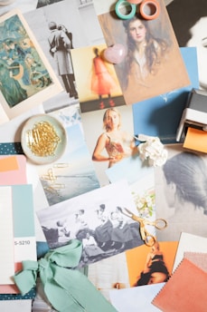 A collage composed of various vintage-style photographs and paintings, including portraits and a black-and-white image of women sitting on a ledge. There are art prints, ribbon, scissors, and decorative items like gold paper clips and pastel washi tape. The collection has a soft and artistic feel.