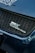 A close-up view of a car's front grille featuring the logo SWK Suzuki Works Kurume. The grille has a honeycomb pattern, and the surrounding areas of the car are a glossy blue color with visible reflections.
