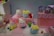 A collection of cute, colorful plush toys is displayed on a set of pink platforms. The toys have large, expressive eyes and resemble popular cartoon characters. Around the toys, there are small, colorful blocks, adding to the vibrant aesthetic.