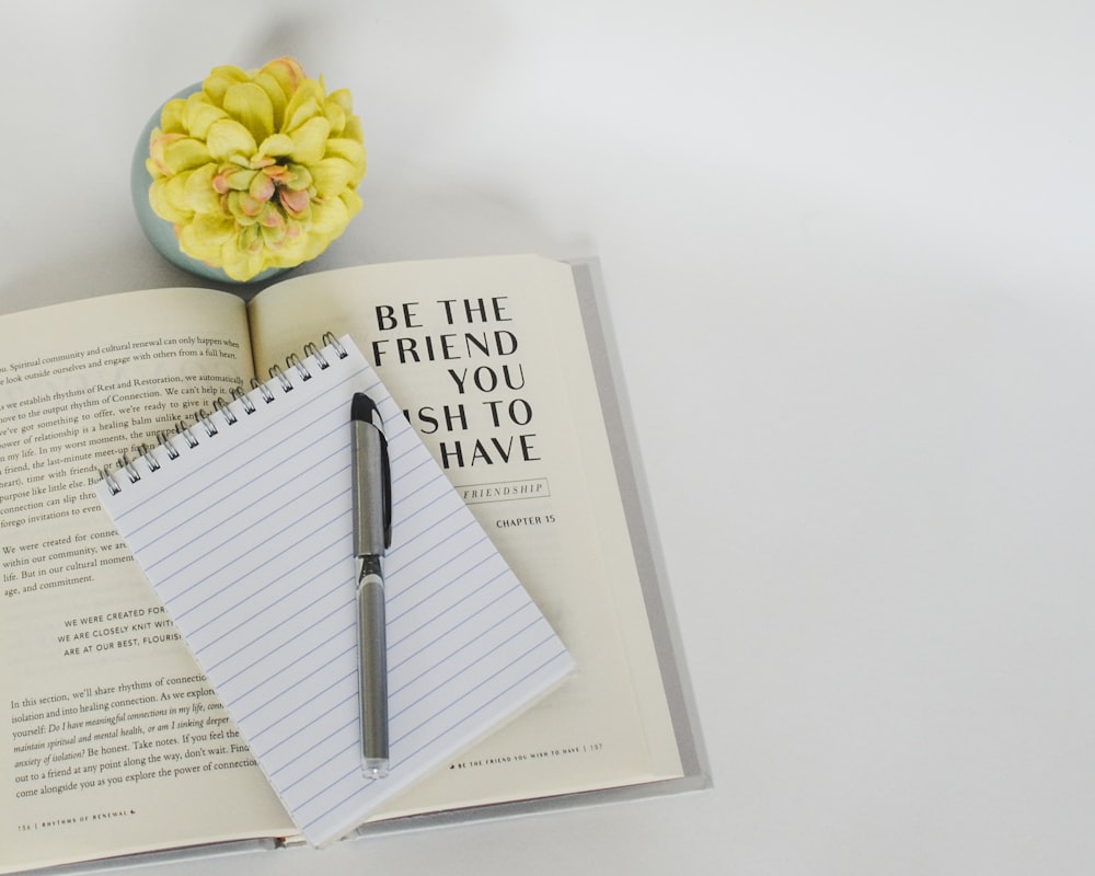 a notebook with a pen on top of it next to a flower