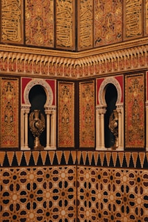 Intricate and ornate architectural details featuring Arabic calligraphy and geometric patterns adorn the walls. The use of arches and detailed carvings adds to the richness of the design, showcasing cultural and artistic expressions.