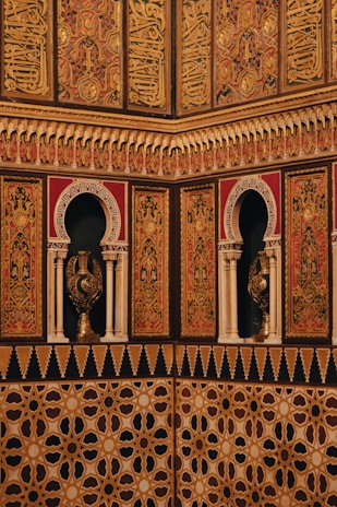 Intricate and ornate architectural details featuring Arabic calligraphy and geometric patterns adorn the walls. The use of arches and detailed carvings adds to the richness of the design, showcasing cultural and artistic expressions.