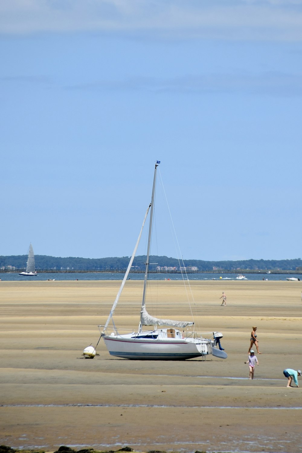 a sailboat on the beach with people standing around it