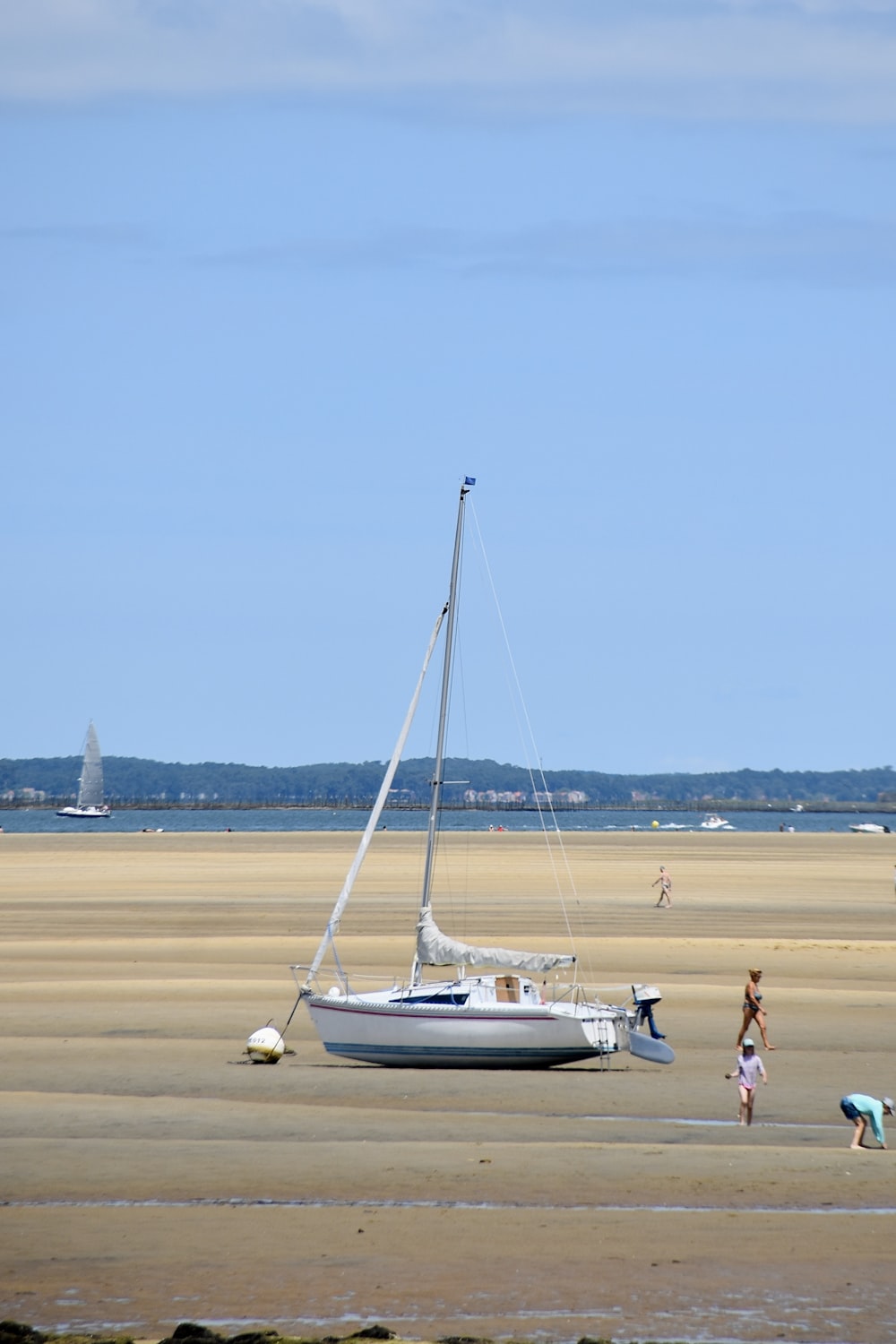 a sailboat on the beach with people standing around it