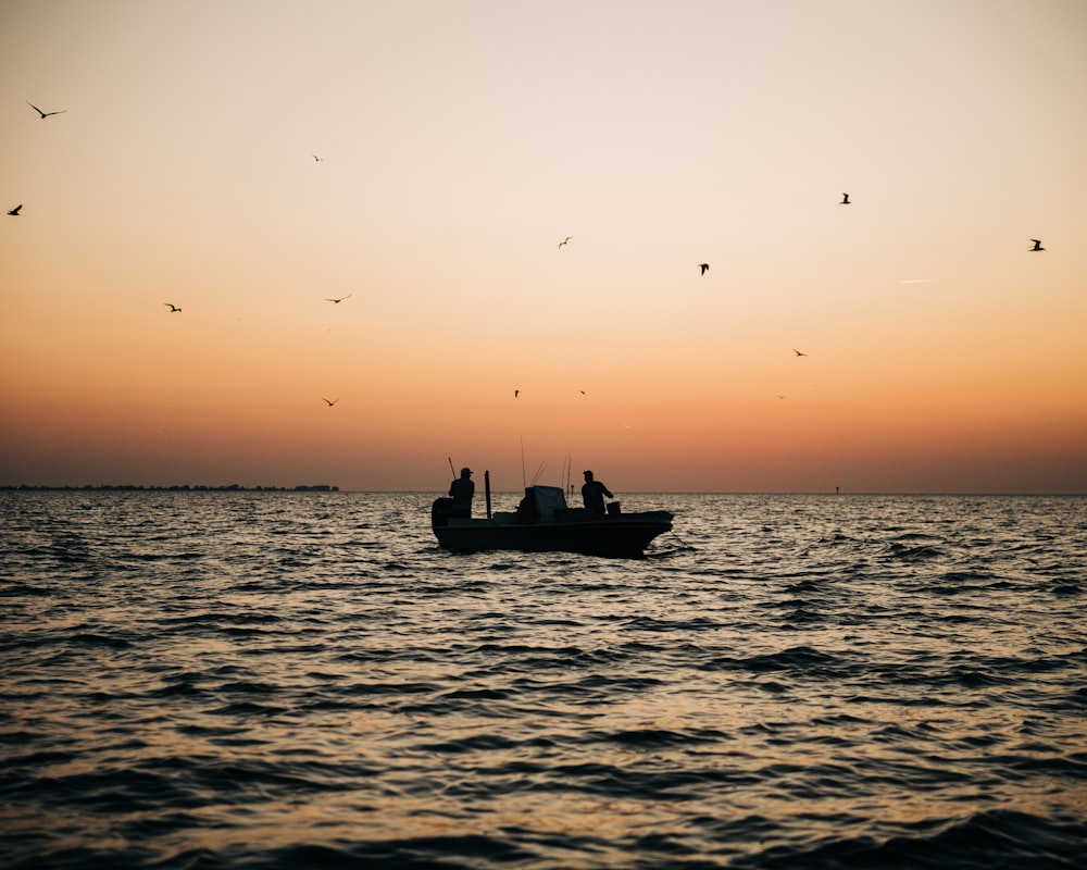 a small boat in the middle of the ocean at sunset
