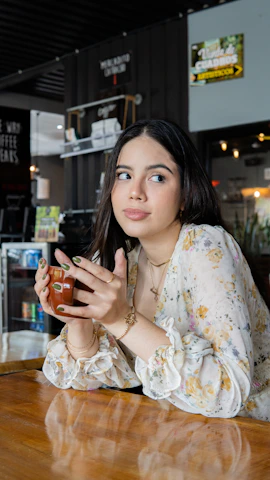 A stylish woman in a flowing cream blouse sitting at a minimalist café table, sipping coffee thoughtfully.