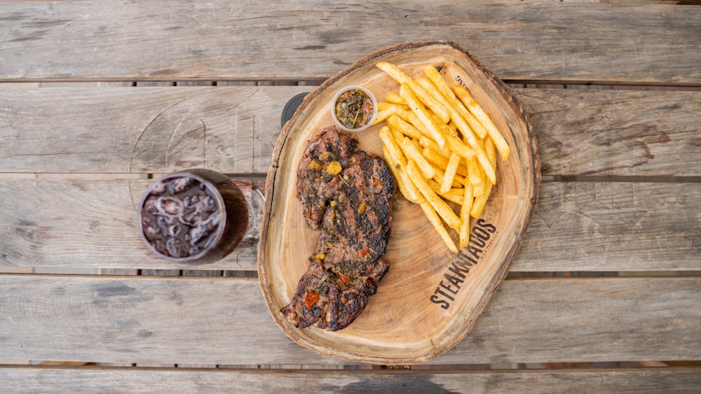 a wooden tray with a steak and french fries on it