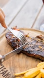 a person cutting a piece of steak with a fork and knife