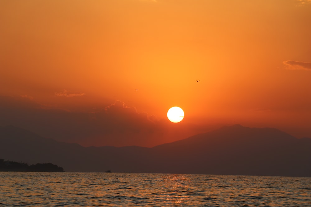 the sun is setting over the water with mountains in the background