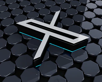 A metallic three-dimensional logo is positioned above a hexagonal tiled surface. The tiles have a glossy finish with a reflective appearance, and the logo features sharp lines and edges, with a futuristic design. Subtle neon blue lighting adds depth and contrast to the composition.