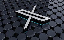 A metallic three-dimensional logo is positioned above a hexagonal tiled surface. The tiles have a glossy finish with a reflective appearance, and the logo features sharp lines and edges, with a futuristic design. Subtle neon blue lighting adds depth and contrast to the composition.