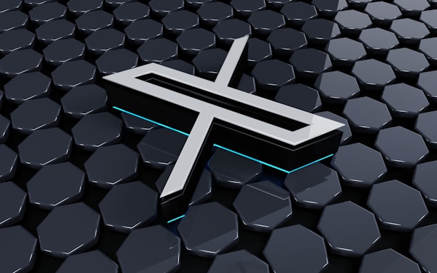 A metallic three-dimensional logo is positioned above a hexagonal tiled surface. The tiles have a glossy finish with a reflective appearance, and the logo features sharp lines and edges, with a futuristic design. Subtle neon blue lighting adds depth and contrast to the composition.