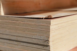 Close-up of skilled hands inspecting a smooth plywood sheet in a warmly lit factory setting.